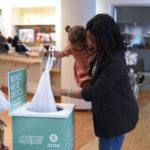 A mother and daughter adding a bag into a recycle dustbin at Mamas & Papas store