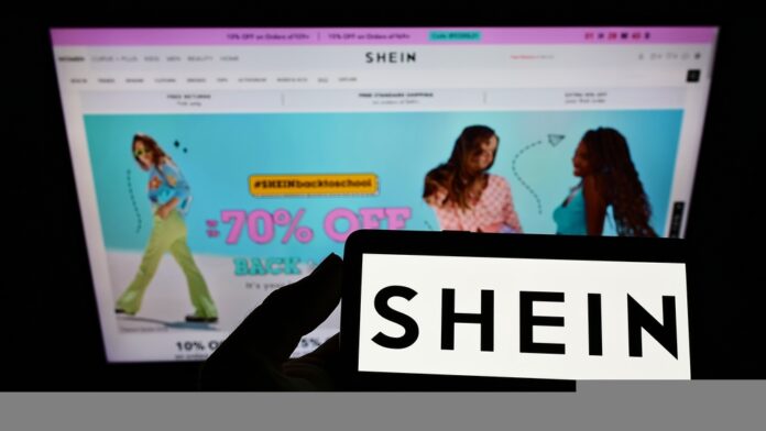 Person holding smartphone with logo of e-commerce company Shein on screen in front of website Focus on phone display